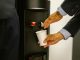 Man in business attire pouring water into a white cup from a dispenser.