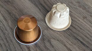 Capsule de café en aluminium posée à côté d'une capsule compostable en fibre végétale