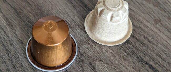 Capsule de café en aluminium posée à côté d'une capsule compostable en fibre végétale