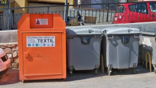 Borne de collecte de textiles usagés à côté de conteneurs à déchets
