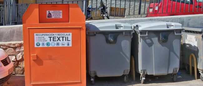 Borne de collecte de textiles usagés à côté de conteneurs à déchets