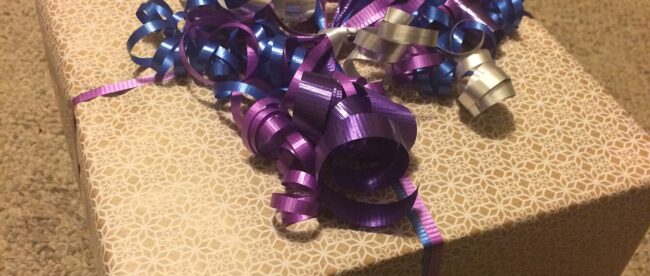 Cadeau emballé dans du papier uni avec un ruban violet frisé
